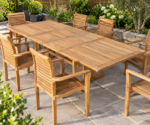 Teak extending garden dining table with eight matching slatted armchairs on a stone patio