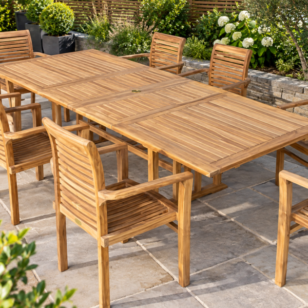 Teak extending garden dining table with eight matching slatted armchairs on a stone patio